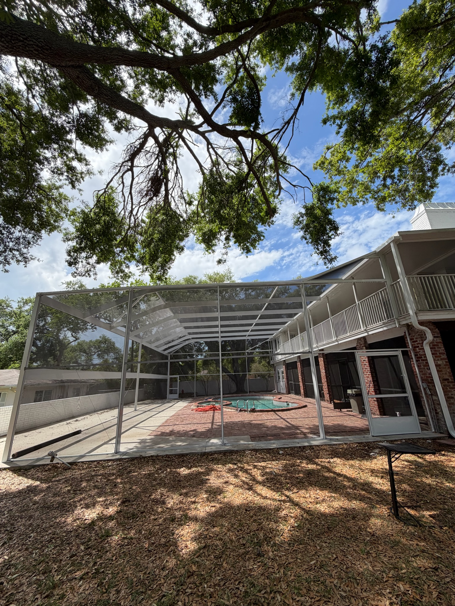 Large white pool screen enclosure beneath oak trees in Florida